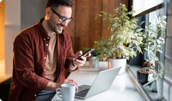 A man working with a laptop and holding a phone.